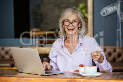 Portrait of senior woman using laptop computer while eating breakfast