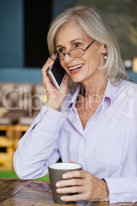 Smiling senior woman talking on smart phone while holding mug