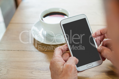 Close up of senior person holding smart phone while sitting at wooden table