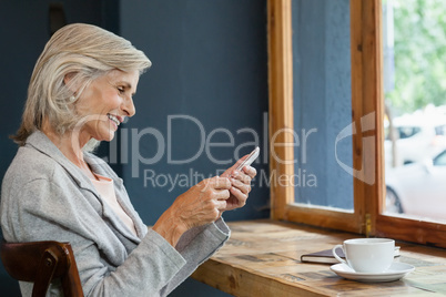 Smiling woman using smart phone while sitting at table