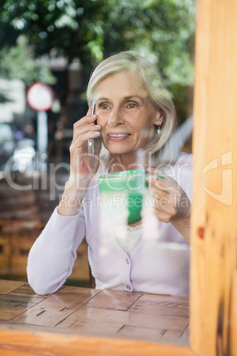 Senior woman drinking coffee while talking on smart phone