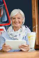 Smiling senior woman holding digital tablet while sitting at table