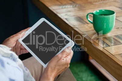 Close up of senior  woman holding tablet against coffee cup on table