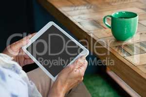 Close up of senior  woman holding tablet against coffee cup on table