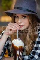 Portrait of young woman wearing hat drinking cold coffee