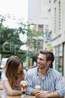 Happy couple laughing while drinking cold coffee at sidewalk cafe