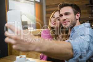 Young couple taking selfie on mobile phone while having coffee