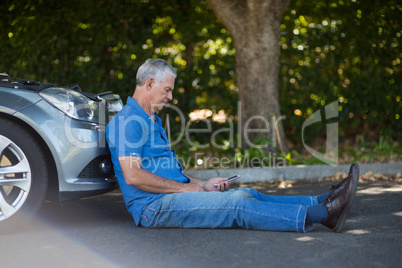 Senior man sitting by car on road