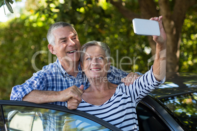 Senior couple taking selfie by car