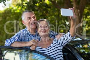 Senior couple taking selfie by car