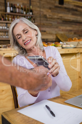 Senior woman making payment through NFC technology on mobile phone