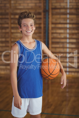Smiling high school boy holding a basketball in the court