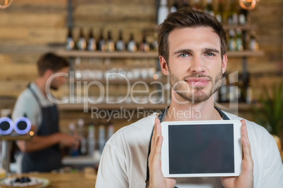 Portrait of smiling waiter showing digital tablet at counter