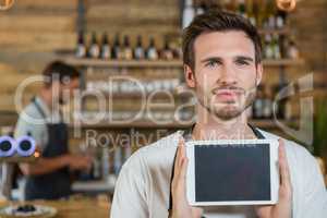 Portrait of smiling waiter showing digital tablet at counter