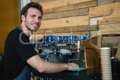 Portrait of smiling waiter cleaning coffee machine at counter