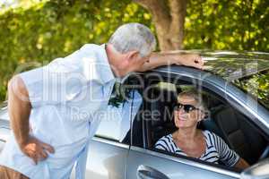 Senior man talking to woman sitting in car