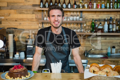 Portrait of smiling waiter leaning at counter