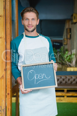 Portrait of smiling waiter holding chalkboard with open sign