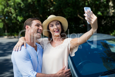 Young couple taking selfie by car