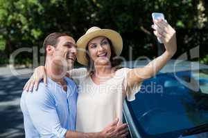 Young couple taking selfie by car