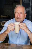 Senior man holding cold coffee while sitting at table