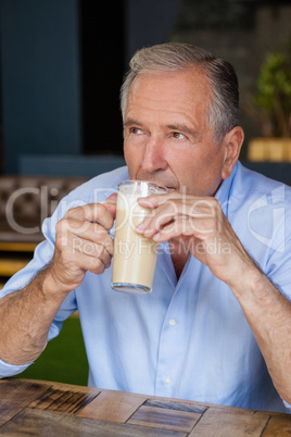 Senior thoughtful man holding cold coffee while sitting at table