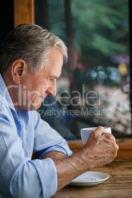 Thoughtful senior man holding coffee cup at table
