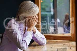 Senior woman covering face while sitting at table in cafe