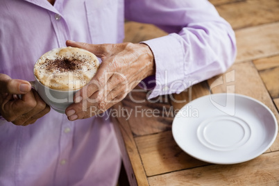 Senior woman holding coffee cup while standing at table