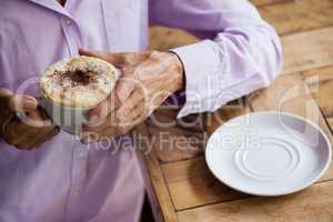 Senior woman holding coffee cup while standing at table