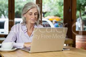 Senior woman drinking coffee while working on laptop at table