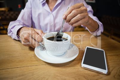 Woman stirring coffee while sitting at table in cafe shop