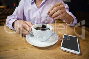 Woman stirring coffee while sitting at table in cafe shop