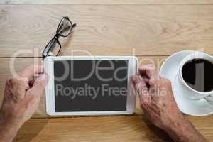 Close up of senior man holding digital tablet while sitting at table