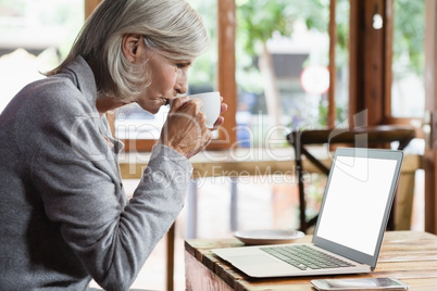 Side view of senior woman drinking coffee while using laptop computer