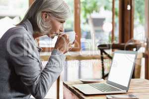 Side view of senior woman drinking coffee while using laptop computer