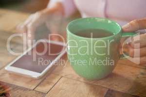 Woman holding cup by smart phone on table