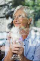 Smiling sneior woman looking away while holding cold coffee