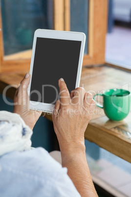 Close up of senior  woman using tablet against coffee cup