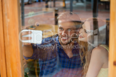 Couple clicking selfie with smart phone while sitting at cafe shop