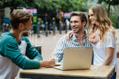 Cheerful couple looking at friend while sitting at sidewalk cafe