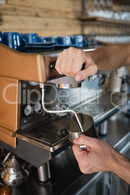 Close-up of waiter hands pouring milk in jug from coffee machine