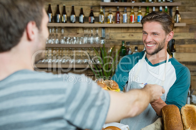 Smiling waiter serving to customer at counter