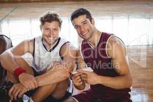 Portrait of smiling basketball players using mobile while relaxing