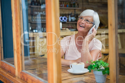 Senior woman talking on mobile phone while having coffee