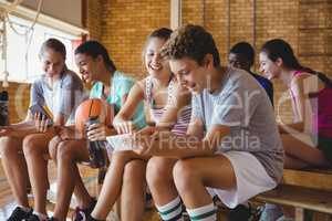 High school kids using mobile phone while relaxing in basketball court