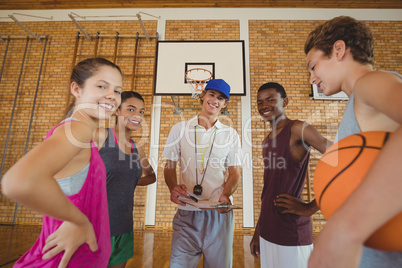 Smiling high school kids and their coach standing in the basketball court