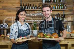 Portrait of waiter and waitresses holding cupcakes and food at counter