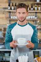 Portrait of smiling waiter serving cup of coffee at counter