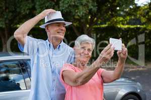 Senior woman taking selfie with man by car